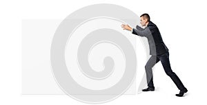 Young businessman is pushing away a big blank banner on white background