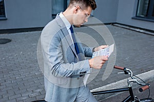 Young businessman reading newspaper near bike