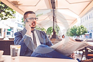 Young businessman reading newspapers and talking on mobile phone