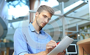 Young businessman reading paperwork at desk in office.