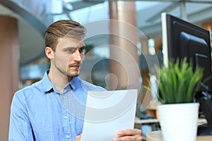 Young businessman reading paperwork at desk in office.