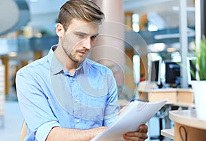 Young businessman reading paperwork at desk in office.