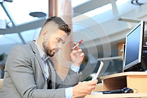 Young businessman reading paperwork at desk in office.