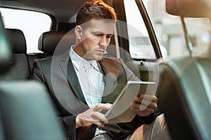 Young businessman reading world daily news while sitting in his car on his way to office, multitasking concept