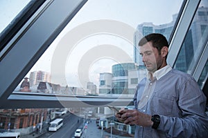 young businessman with a serious face is browsing the news on a mobile phone against the background of a paned window on a high f