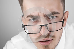 young businessman in shirt and glasses standing and looking at camera  shocked on gray studio background