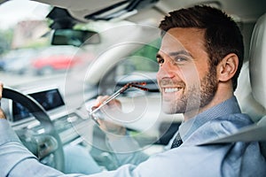 Young businessman with shirt sitting in car. Shot through glass.