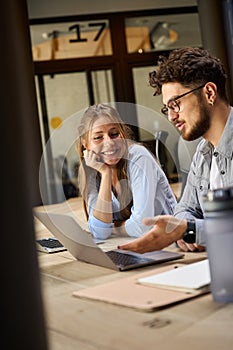 Young businessman showing something on laptop to smiling female colleague