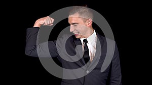 Young businessman shows biceps on his arm. Man in a black suit on a black background