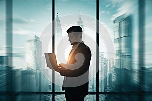 Young businessman silhouette using laptop while standing on creative corporate interior background with panoramic windows and city