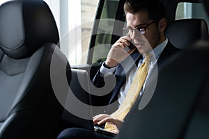 Young businessman sitting on back seat of the car, while his chauffeur is driving automobile. photo