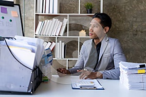 Young businessman sitting at desk with stack of papers facing window, business accounting concept