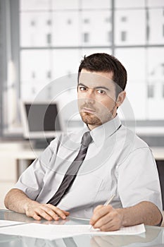 Young businessman sitting at desk writing notes