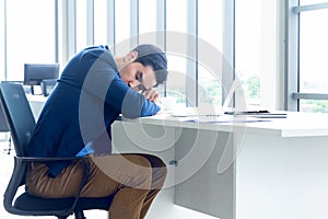 A young businessman sitting in a modern office. He has a feel sleepy because  hard work so tired weary fatigued and exhausted. On