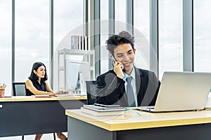 Young businessman sitting at office talking on mobile phone, sitting at desk, using laptop, smiling