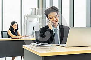 Young businessman sitting at office talking on mobile phone, sitting at desk, using laptop, smiling, businesswoman working