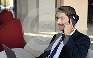 Young businessman sitting relaxed on sofa at hotel lobby making a phone call, waiting for someone.