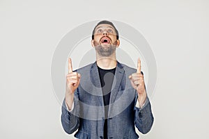 Young businessman with a smile man with a beard in a jacket, amazed and surprised, looking up and pointing with his fingers and