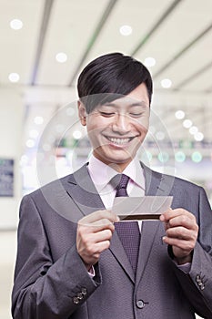 Young businessman smiling and looking down at airplane ticket at the airport, Beijing