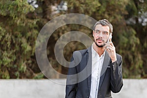 Young businessman speaks by phone on a blurred background of trees