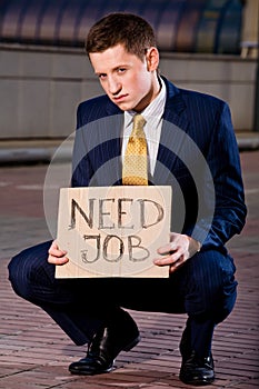 Young businessman squatting with sign Need Job