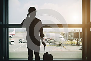 Young businessman stand at terminal in internatianal airport during sunset and talking on the phone to inform them of their