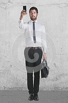 Young businessman standing with briefcase and working with smartphone.