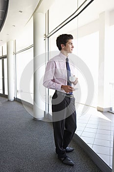 Young Businessman Standing In Corridor Of Modern Office Building Drinking Coffee