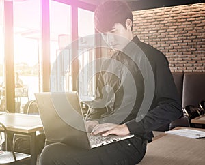 Young businessman standing at desk, working with laptop computer on the edge of a table in the office, concentrating