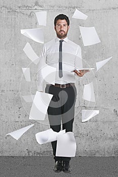 Young businessman standing with flying papers.