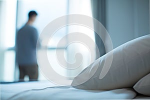 Young businessman standing at hotel window looking out. Bed made up with white pillows and bed sheets in cozy room.