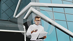 A young businessman stands at the office with a folder of documents in his hands.