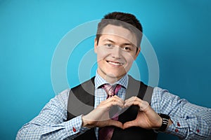 Young businessman in suit on blue background showing heart symbol, sign of love