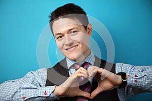 Young businessman in suit on blue background showing heart symbol, sign of love