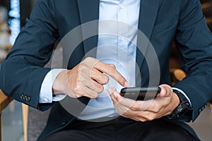 Young Businessman in suit holding and using smartphone for sms messages, man typing touchscreen mobile phone in office or cafe.