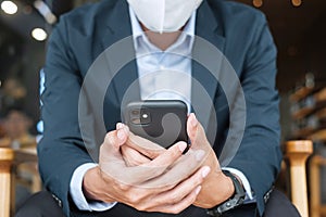 Young Businessman in suit wearing surgical face mask and using smartphone, man typing touchscreen mobile phone in office or cafe.