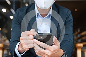 Young Businessman in suit wearing surgical face mask and using smartphone, man typing touchscreen mobile phone in office or cafe.