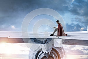 Young businessman super hero on edge of airplane wing
