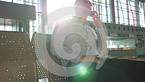 Young businessman talking on phone at airport with sun flare at background. Close up portrait of handsome business man