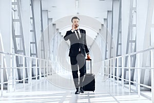 Young businessman talking on phone, walking with luggage in airport