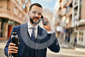 Young businessman talking on the smartphone and holding bottle of water at the city