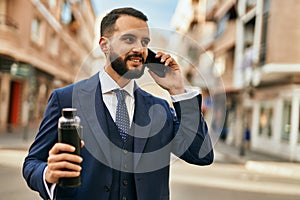 Young businessman talking on the smartphone and holding bottle of water at the city