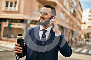 Young businessman talking on the smartphone and holding bottle of water at the city