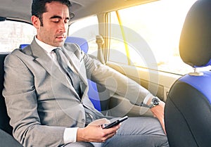 Young businessman in taxi cab and texting sms with smartphone