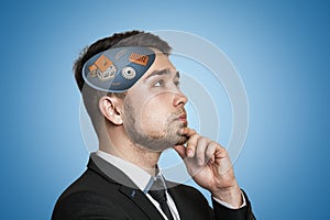 Young businessman thinking with white house, gear wheels, bricks, coil springs in his head on blue background