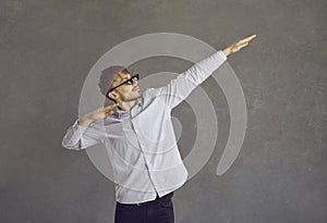 Young businessman in thug life glasses dancing dab against grey studio background