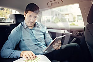 Young businessman travelling into a limo while checking papers and using a tablet