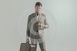 Young businessman unbuttoning suit while holding luggage