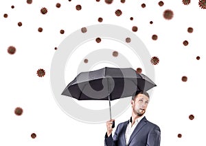 Young businessman under umbrella among coronavirus cells.
