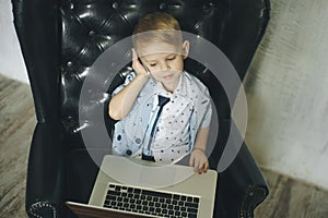 Young businessman using a laptop. funny child in glasses. Fashion portrait of little handsome boy in office